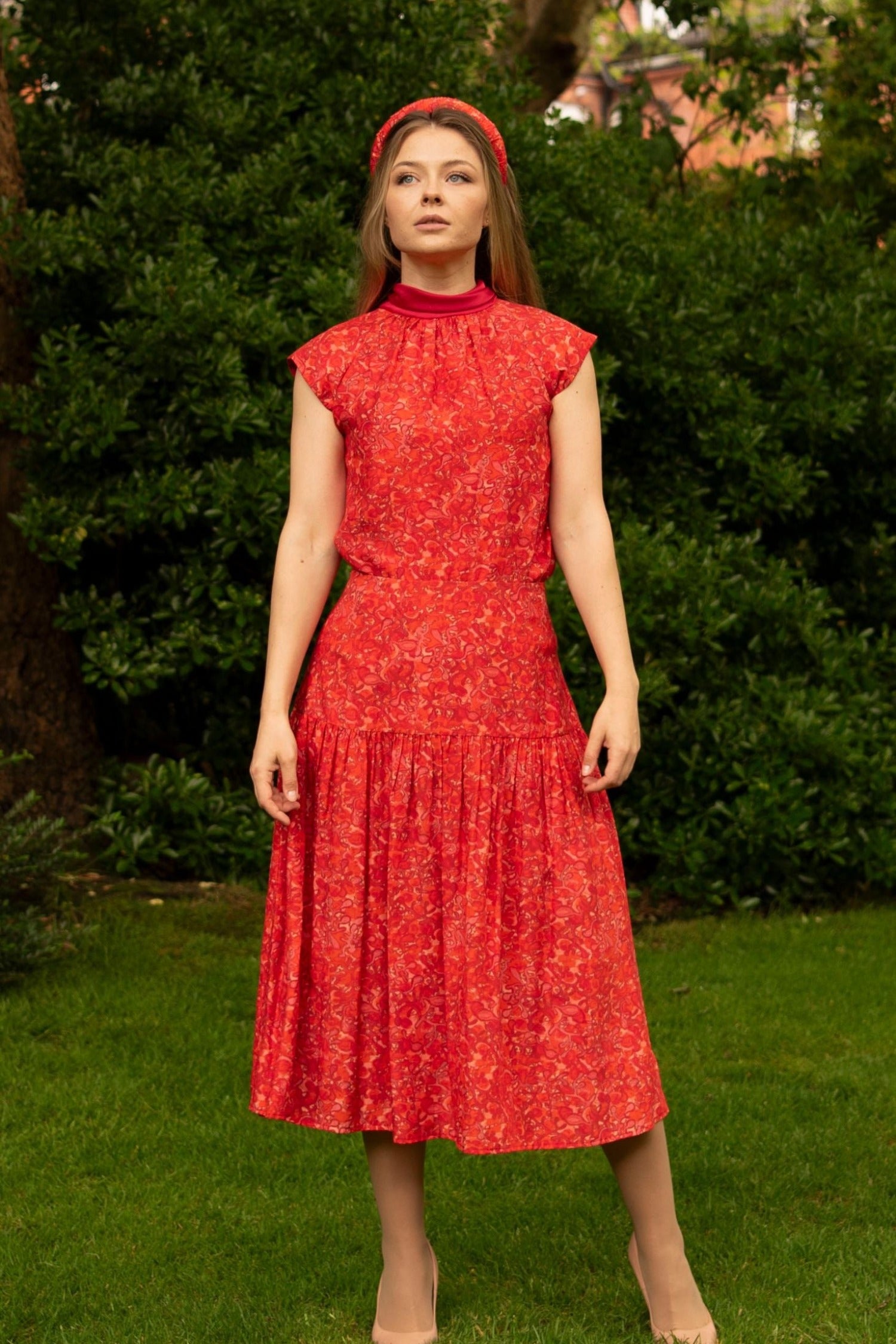 Model wearing a-line midi silk bamboo skirt with an extra wide waistband and gathered detail from hips down in vibrant red swirl print, worn with matching halter neck cap sleeve Maya top and padded headband.