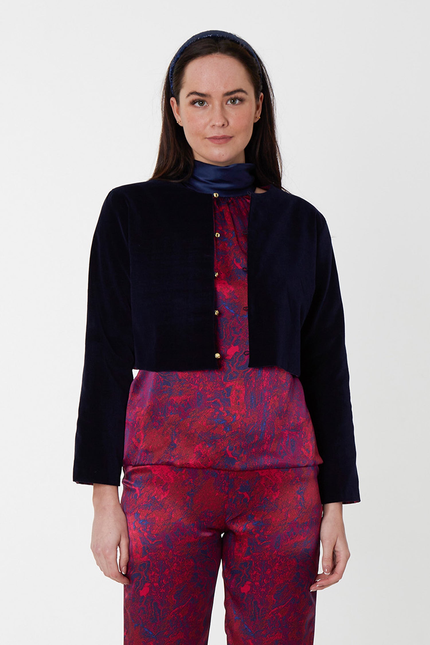 Model wearing reversible box shaped cropped navy velvet jacket, with silver bell fastening, worn with Sophie Top and Georgia Trousers in Fire Ocean, and navy headband.