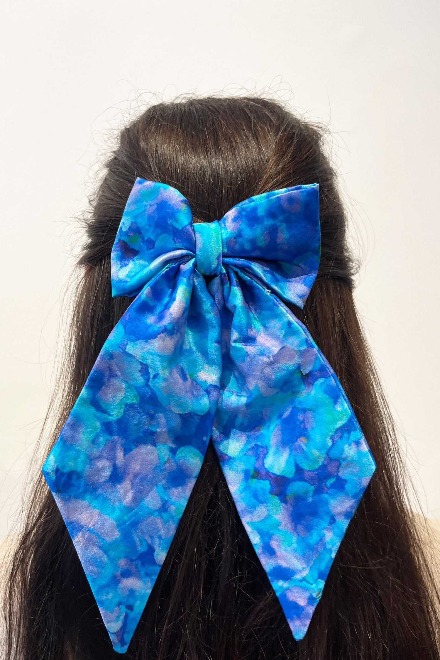 Model wearing silk satin turquoise print bow with ribbon styling and silver hair clip.
