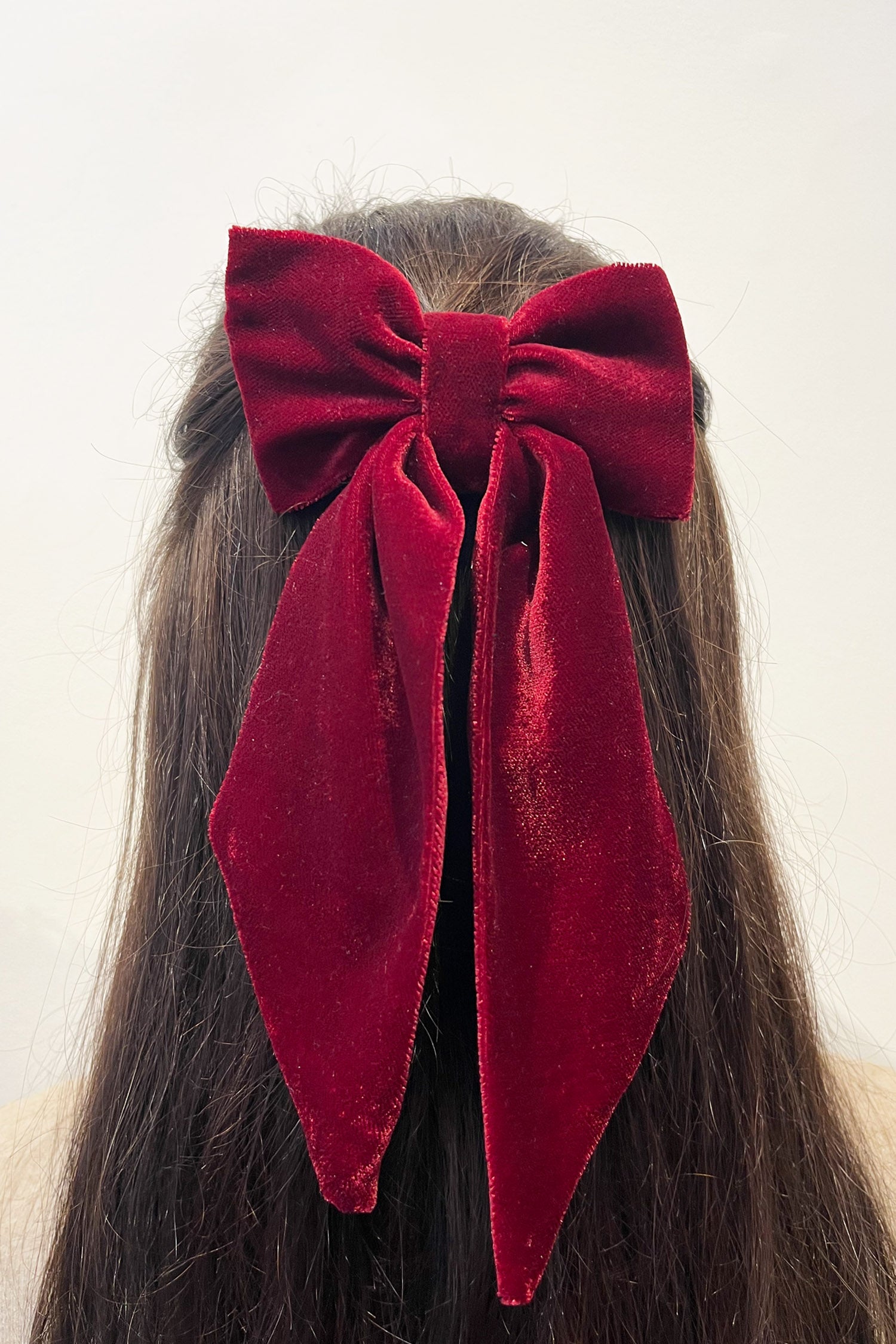 Model wearing burgundy velvet bow with ribbon styling and silver hair clip.