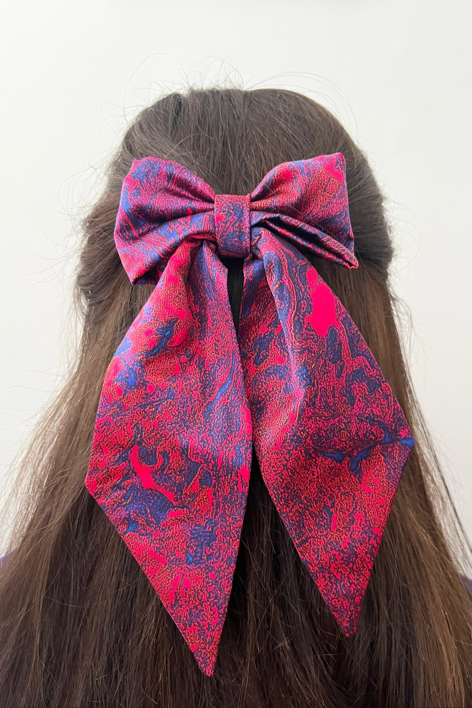 Model wearing red marble print silk satin bow with ribbon styling and silver hair clip.