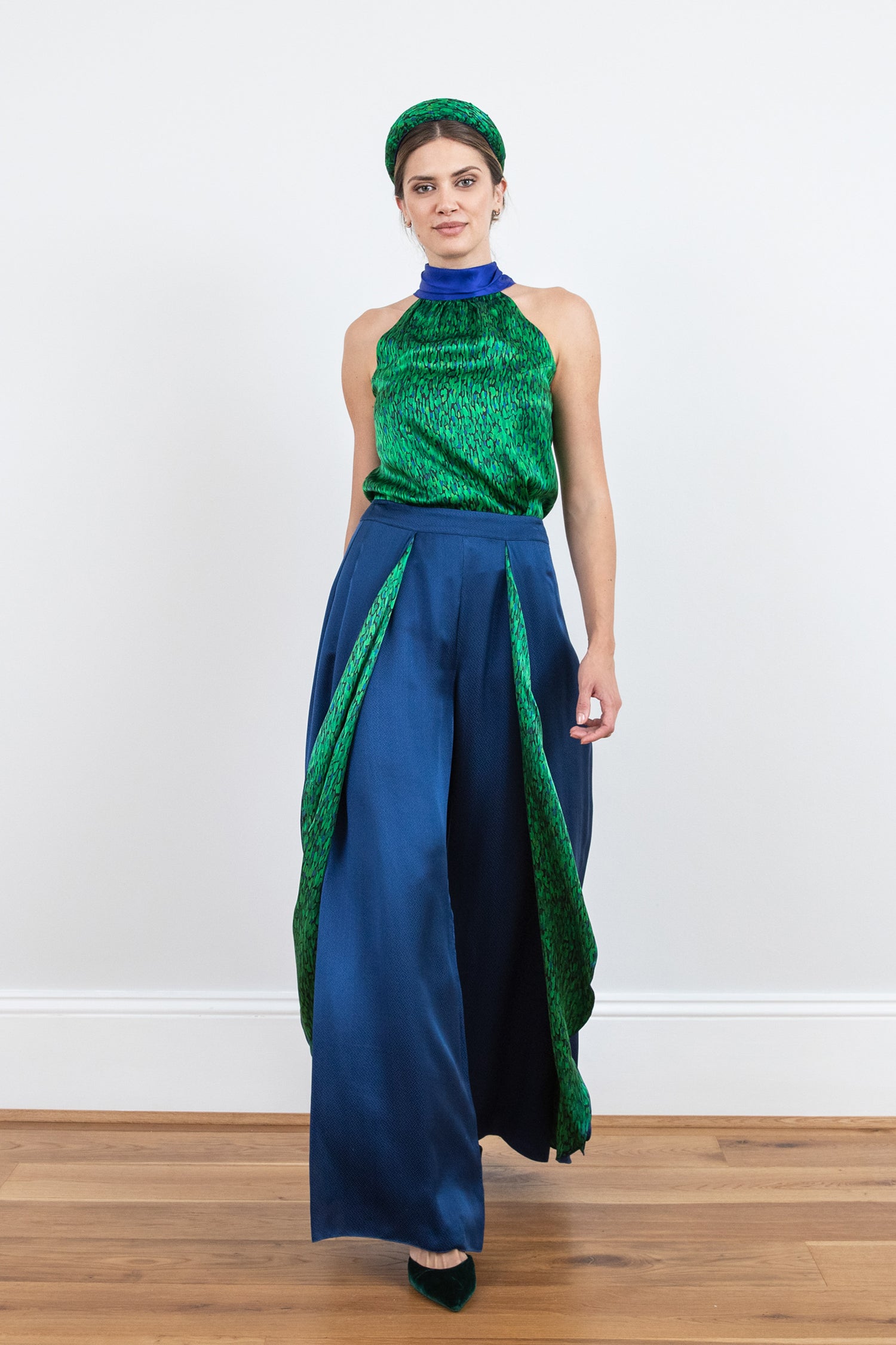 Model wearing an Isabel Manns wide leg wrap around style silk viscose trousers in navy and contrasting vibrant green print lining, worn with matching halterneck Sophie Top in vibrant green print and padded headband.