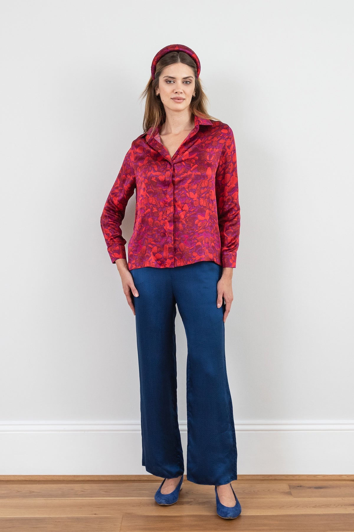 a red pebble inspired printed silk satin shirt worn effortlessly by a model with a matching padded headband and navy trousers with her arm on her hip