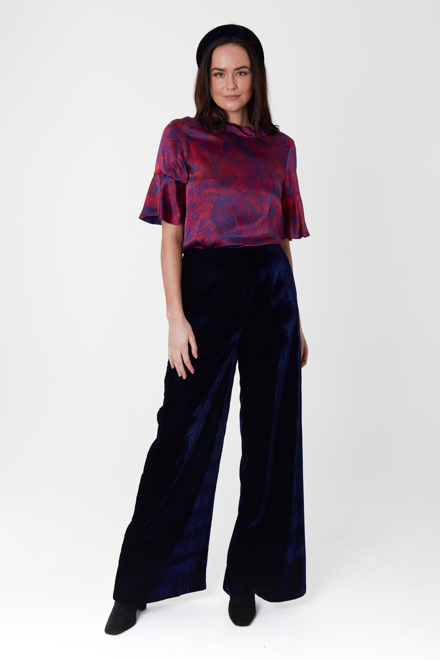 Model wearing high waisted palazzo pants in navy velvet, worn with matching padded headband and reversible peplum sleeve silk satin Rosie top in red marble print.