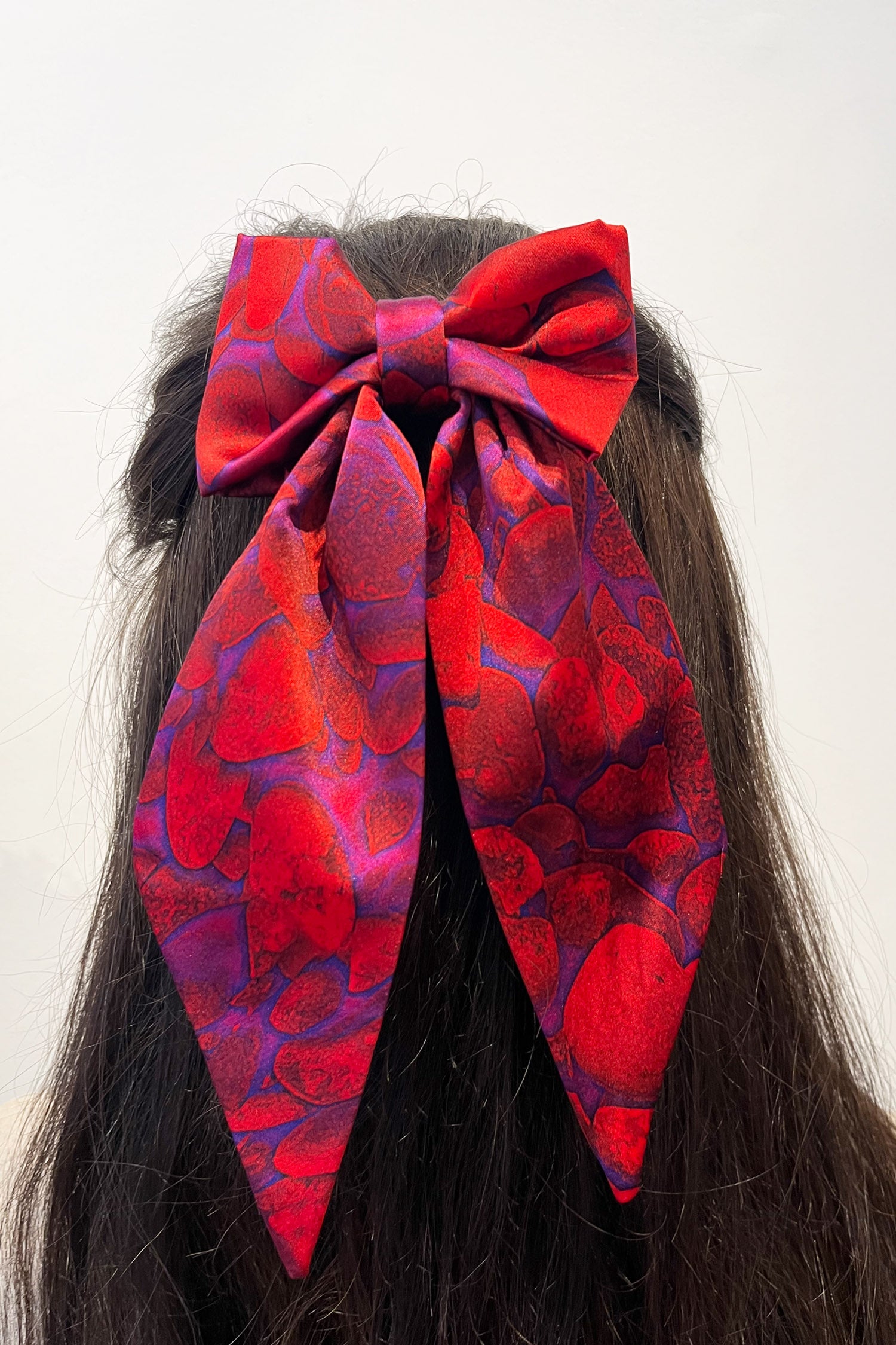 Model wearing vibrant red printed silk satin bow with ribbon styling and silver hair clip.