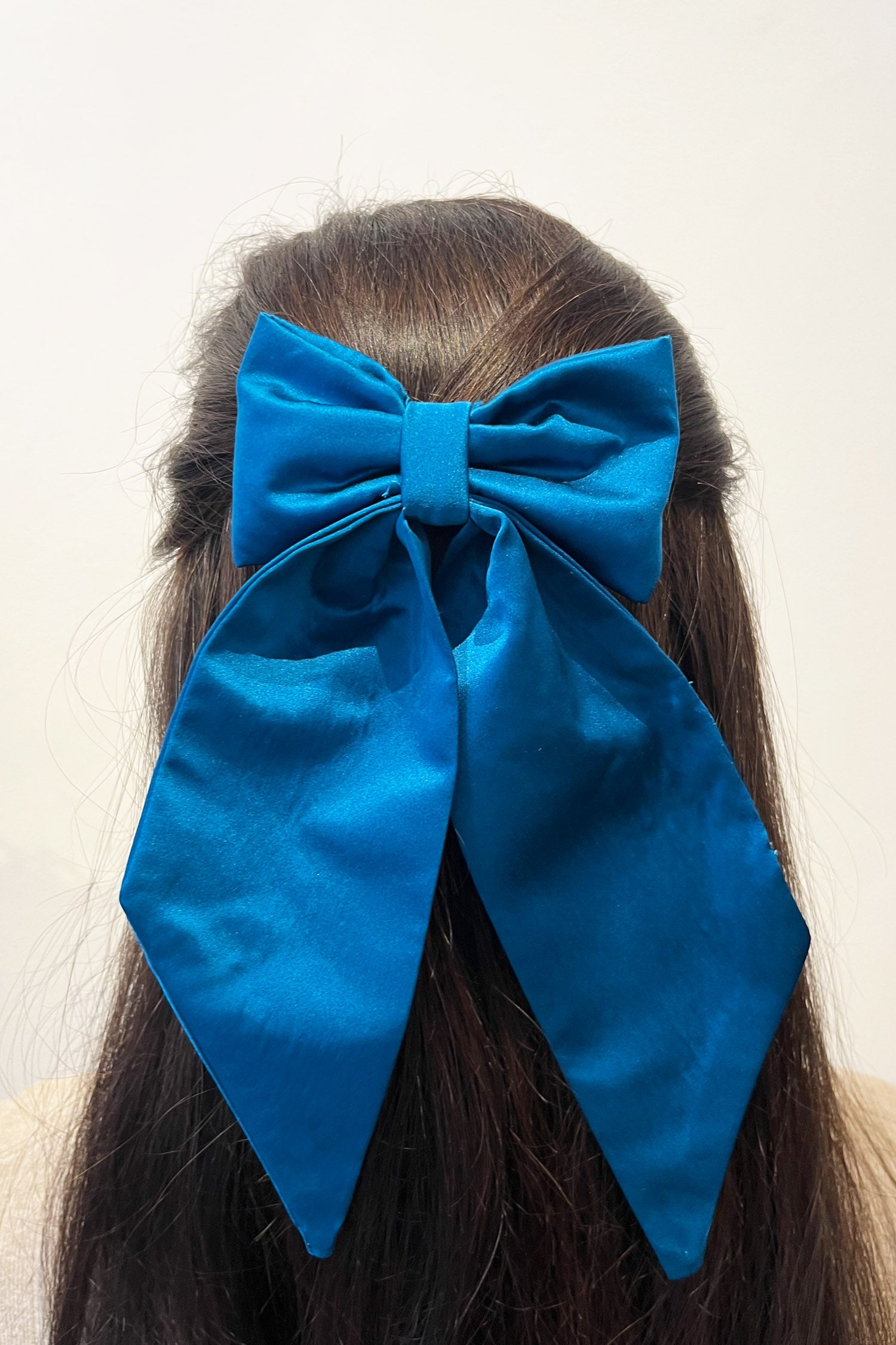 Model wearing silk satin teal bow with ribbon styling and silver hair clip.