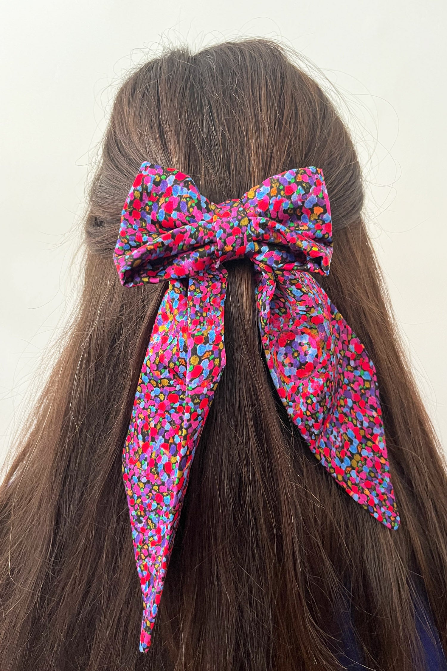 Model wearing purple dotted printed silk satin bow with ribbon styling and silver hair clip.