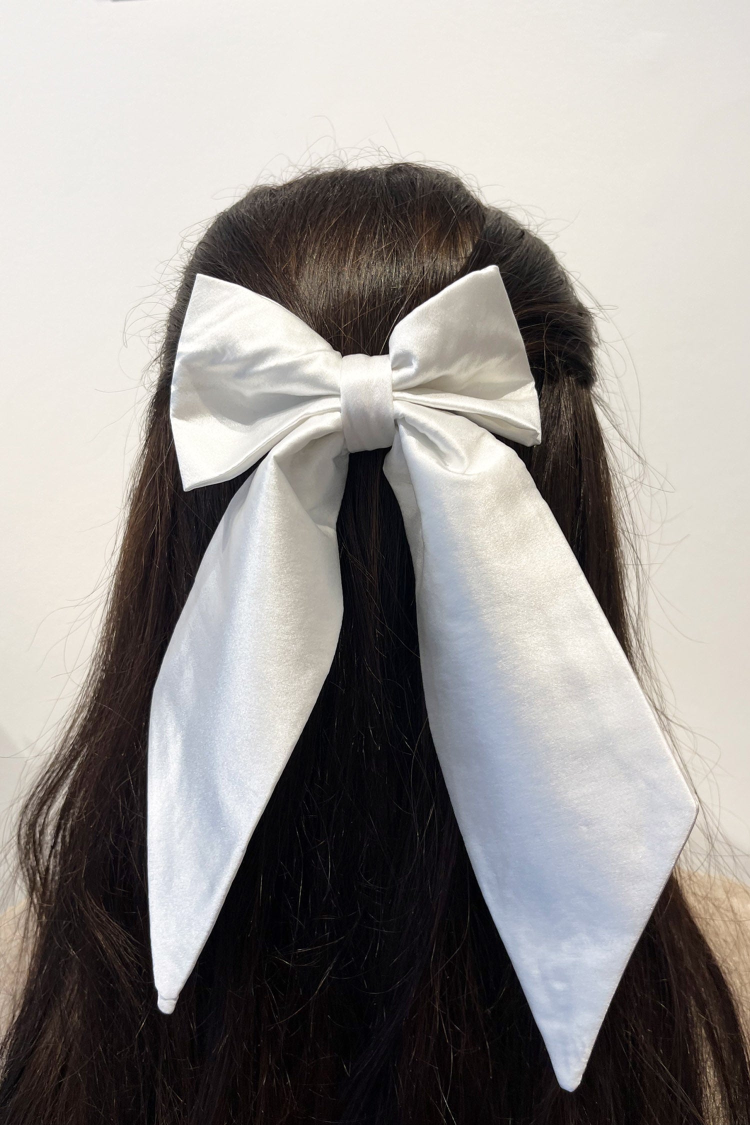 Model wearing white silk satin bow with ribbon styling and silver hair clip.