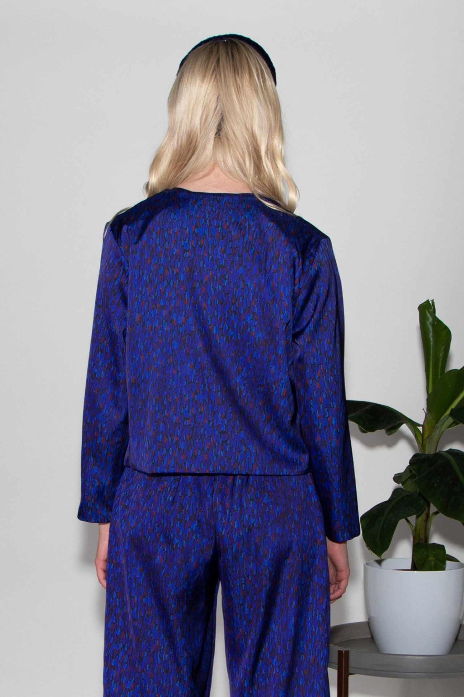 Back view of model wearing reversible box shaped cropped dark blue silk satin/navy velvet jacket, with silver bell fastening, worn with matching Penny Jumpsuit and navy velvet padded headband.