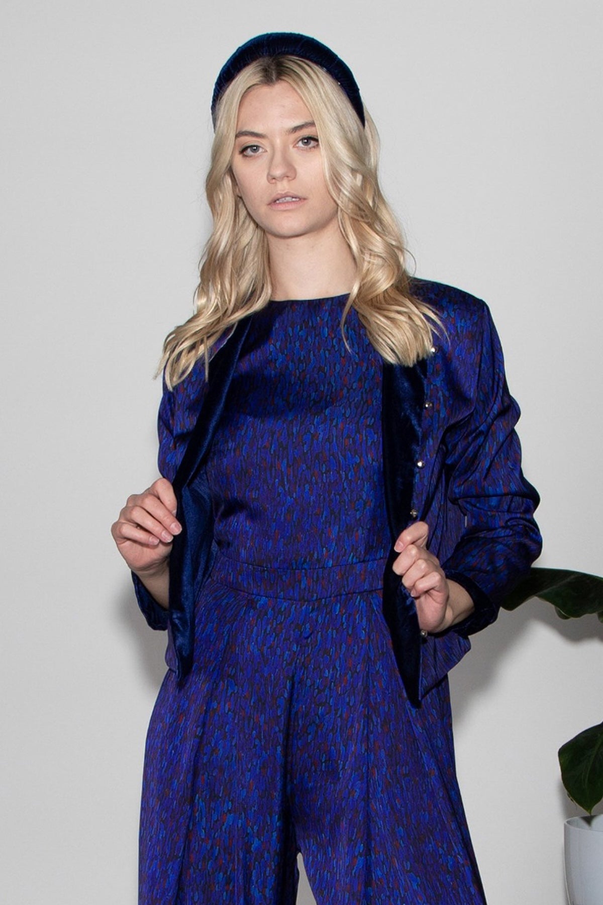 Model wearing reversible box shaped cropped dark blue silk satin/navy velvet jacket, with silver bell fastening, worn with matching Penny Jumpsuit and navy velvet padded headband.