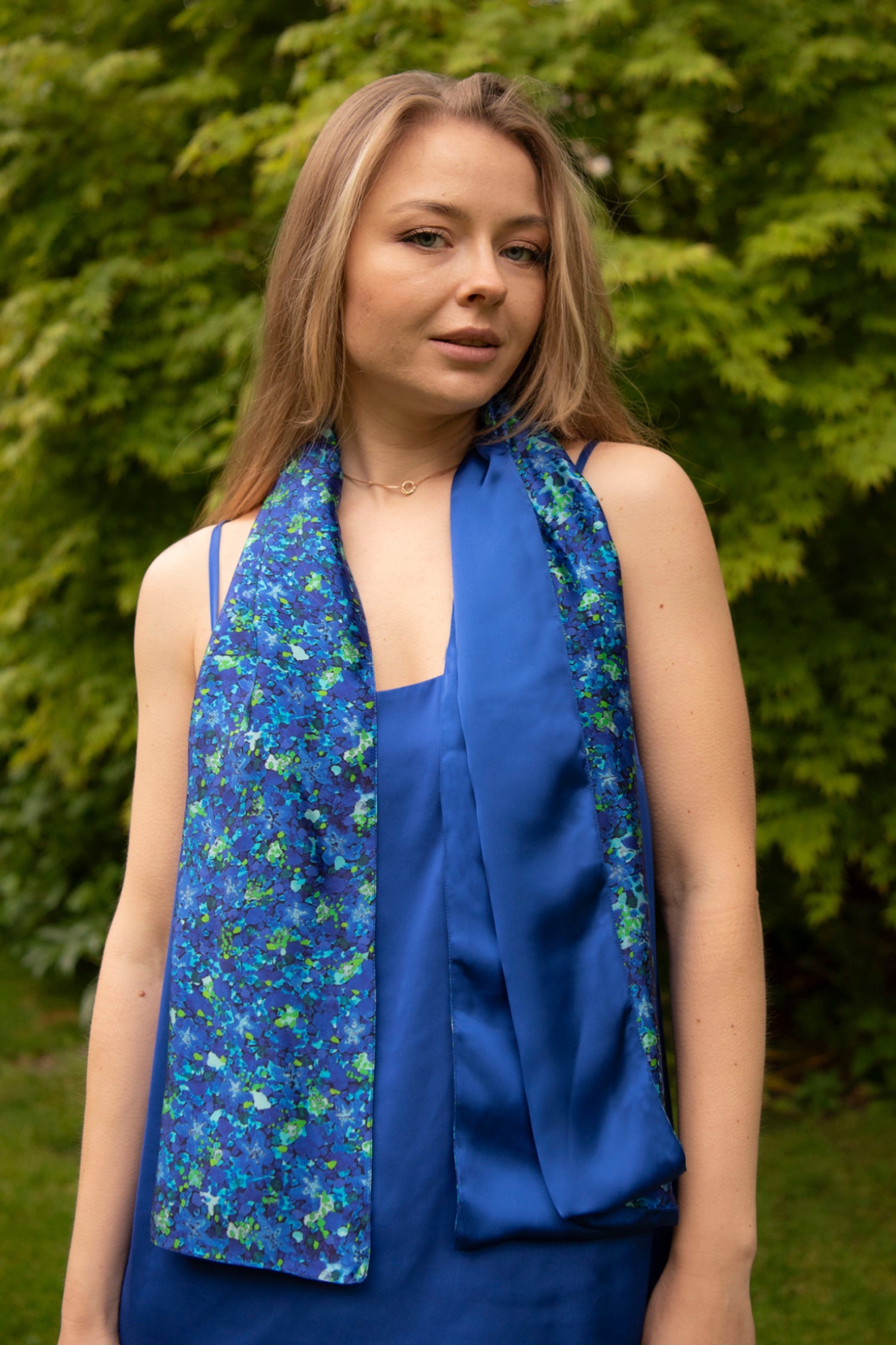 Model wearing long reversible silk satin scarf in blue floral print and cobalt.