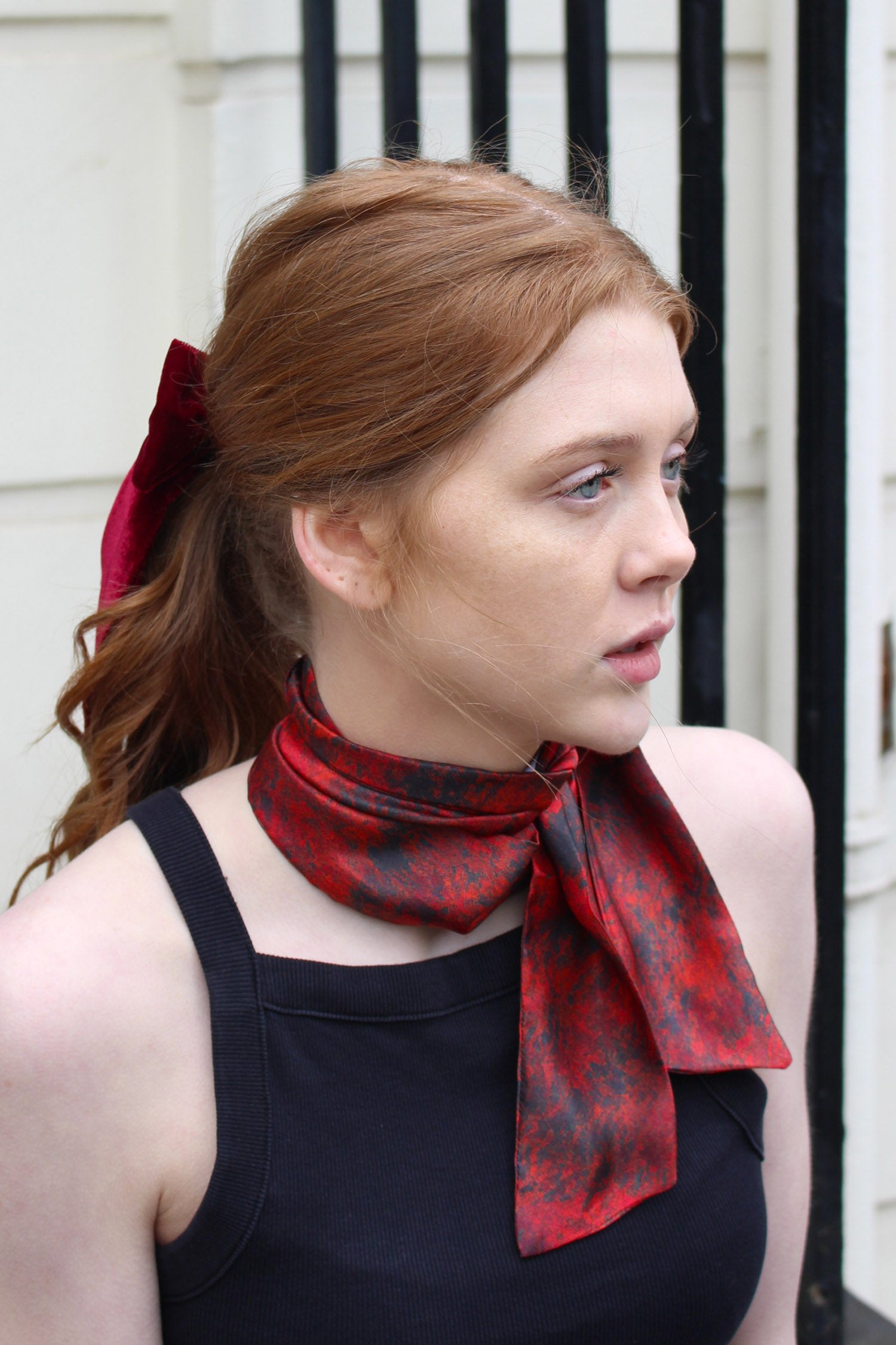 Model wearing narrow silk satin scarf in red print, worn with raspberry pink bow and black vest.