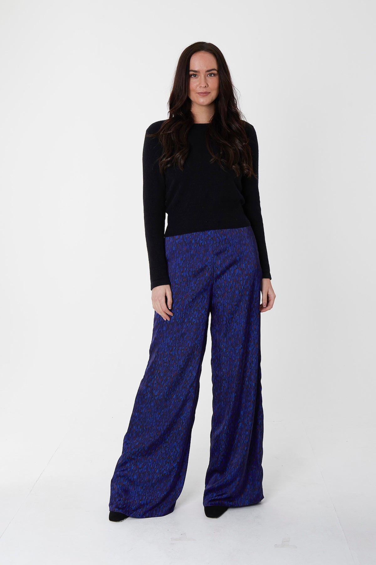 Model wearing reversible high waisted wide palazzo pants in dark blue silk satin print, worn with black high neck jumper.