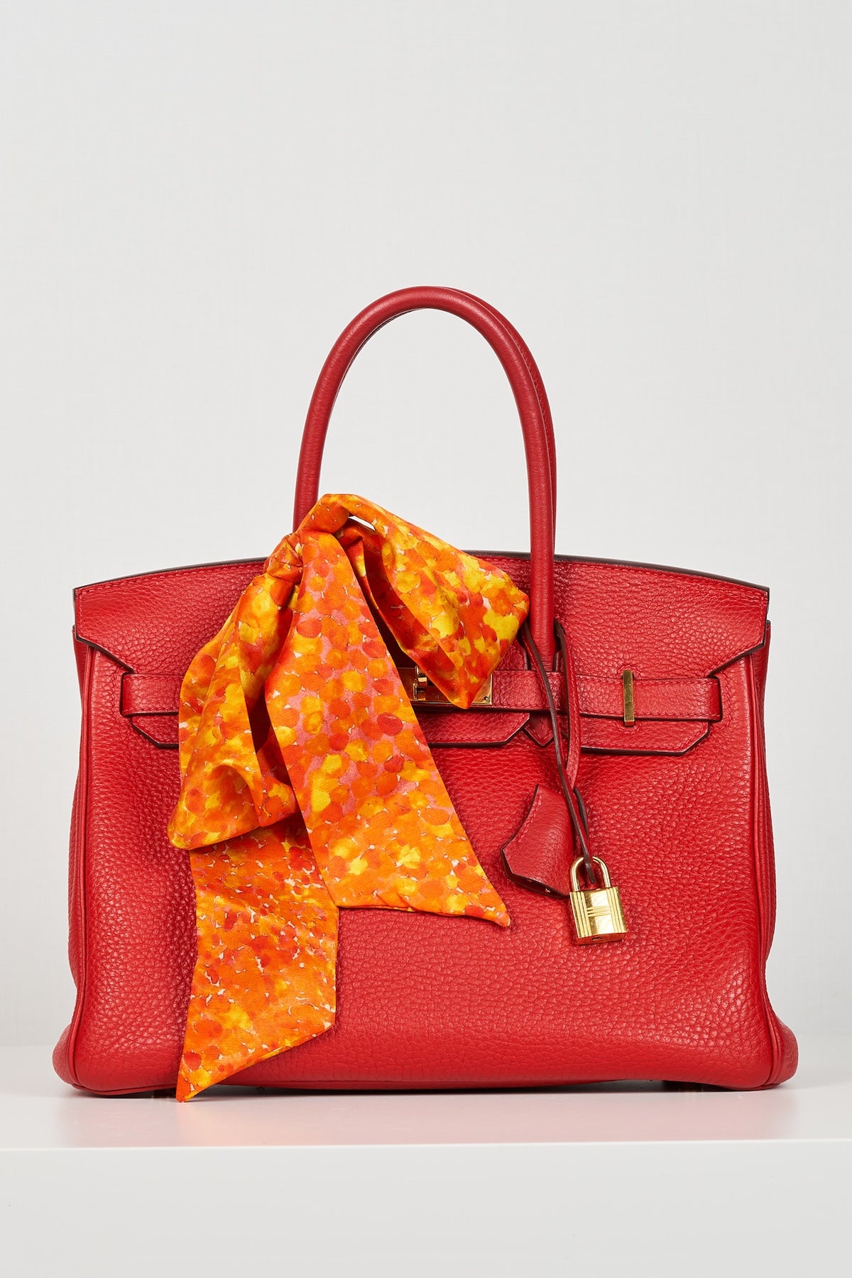 a orange printed skinny scarf accessorised on a birkin bag in a bow