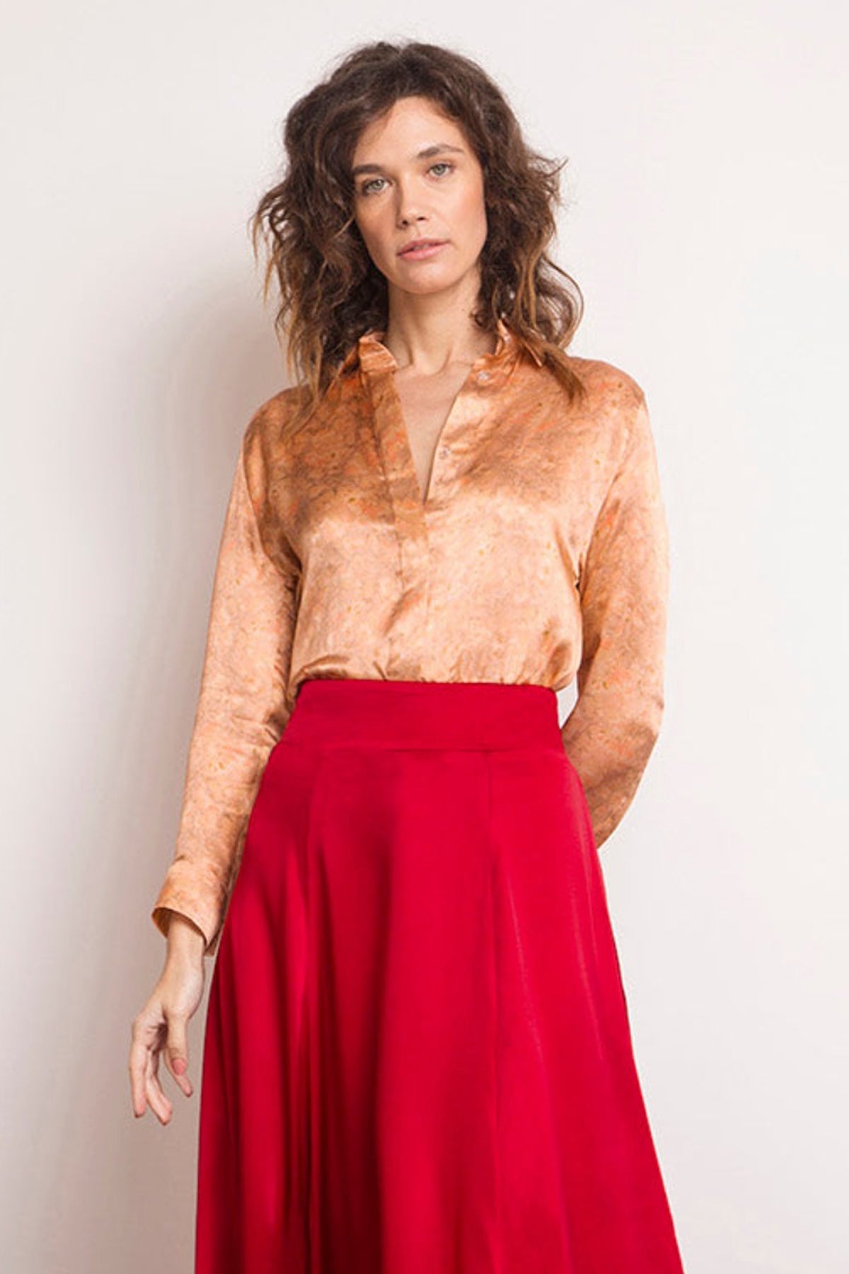 a subtle nude coloured silk satin classic shirt worn by a women with a red silk satin skirt