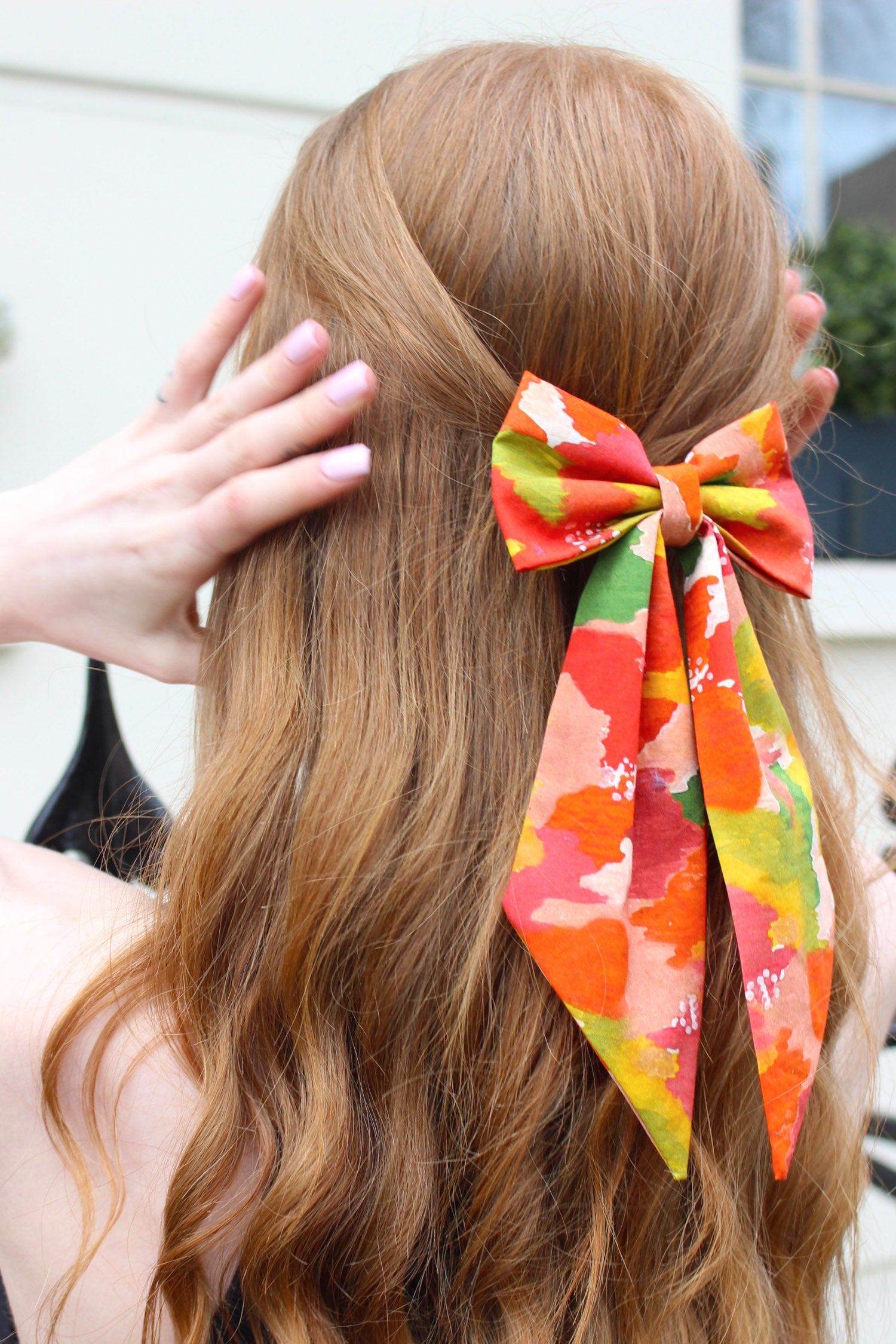 Side view of model wearing multicoloured print silk cotton bow with ribbon styling and silver hair clip.