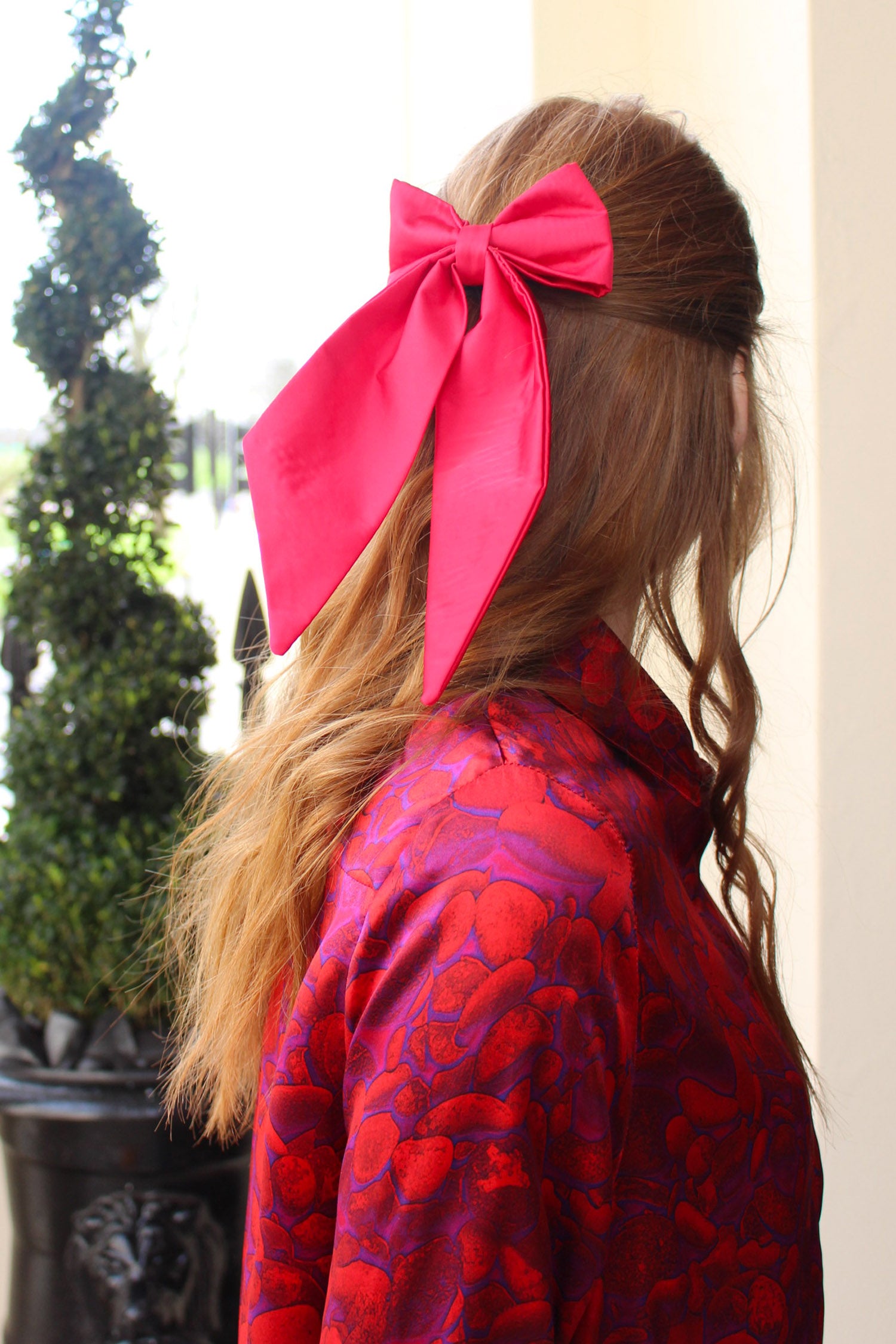 Side view of model wearing Raspberry Pink silk satin bow with ribbon styling and silver hair clip.