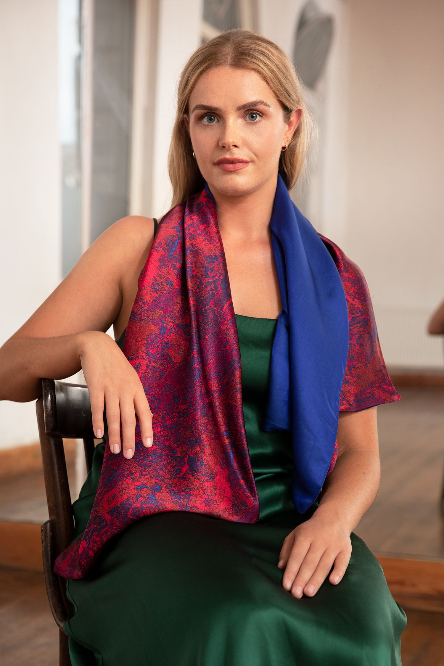 Model wearing long reversible silk satin scarf in red marble print and cobalt, with forest green Alice Dress.