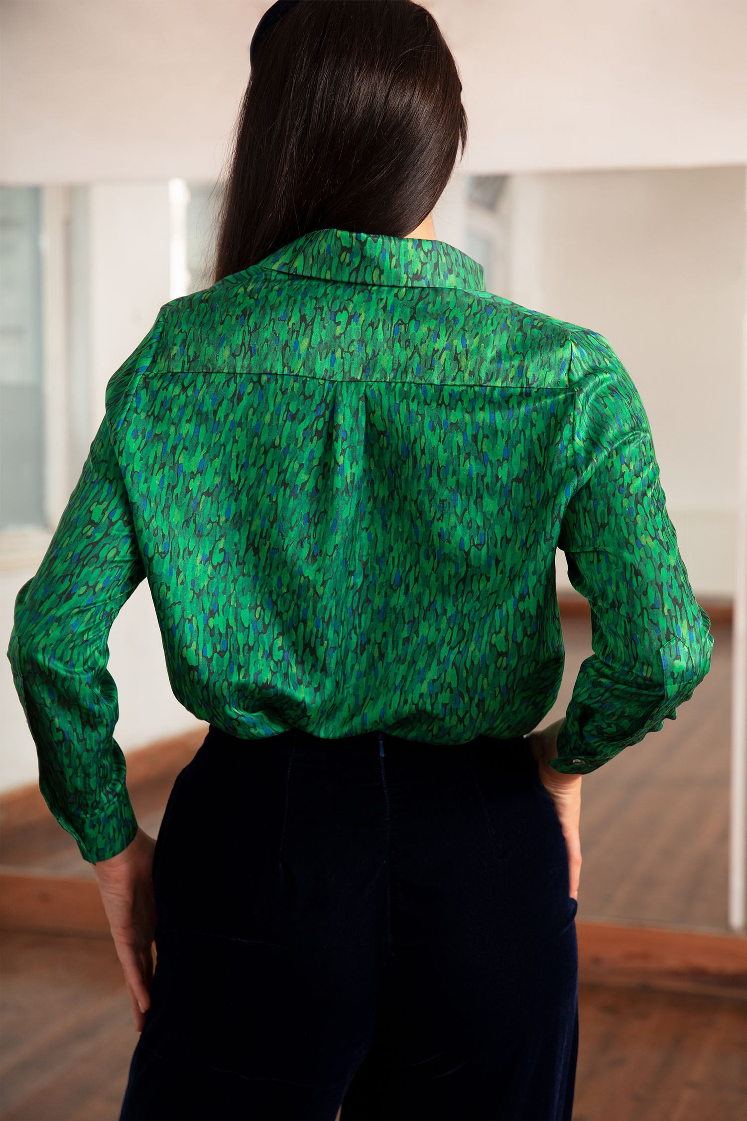 a green printed silk cotton shirt worn by a model with navy velvet trousers and matching headband that is all made in London back view