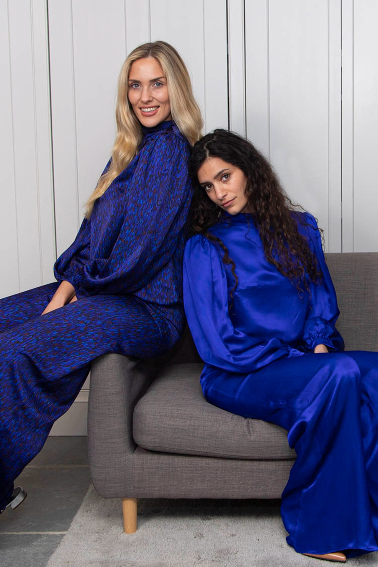 Two models, one wearing reversible high waisted wide palazzo pants in dark blue silk satin print and matching long sleeved Kelly Top, and another wearing reversible high waisted wide palazzo pants in cobalt and matching long sleeved Kelly Top.