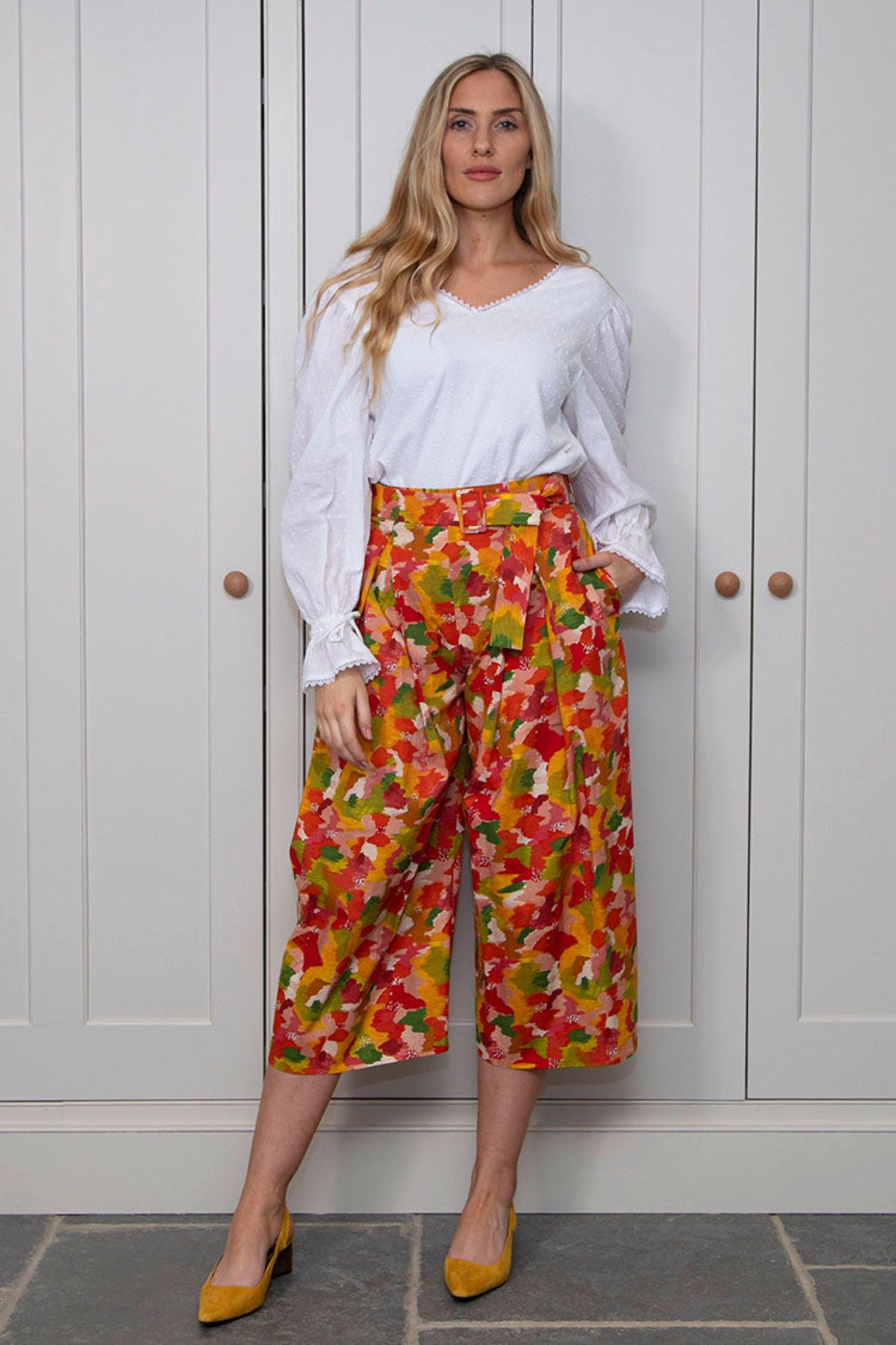 Model wearing high waisted, box pleated ¾ length silk cotton culottes in multi coloured yellow print, worn with white long sleeve Maisie top.