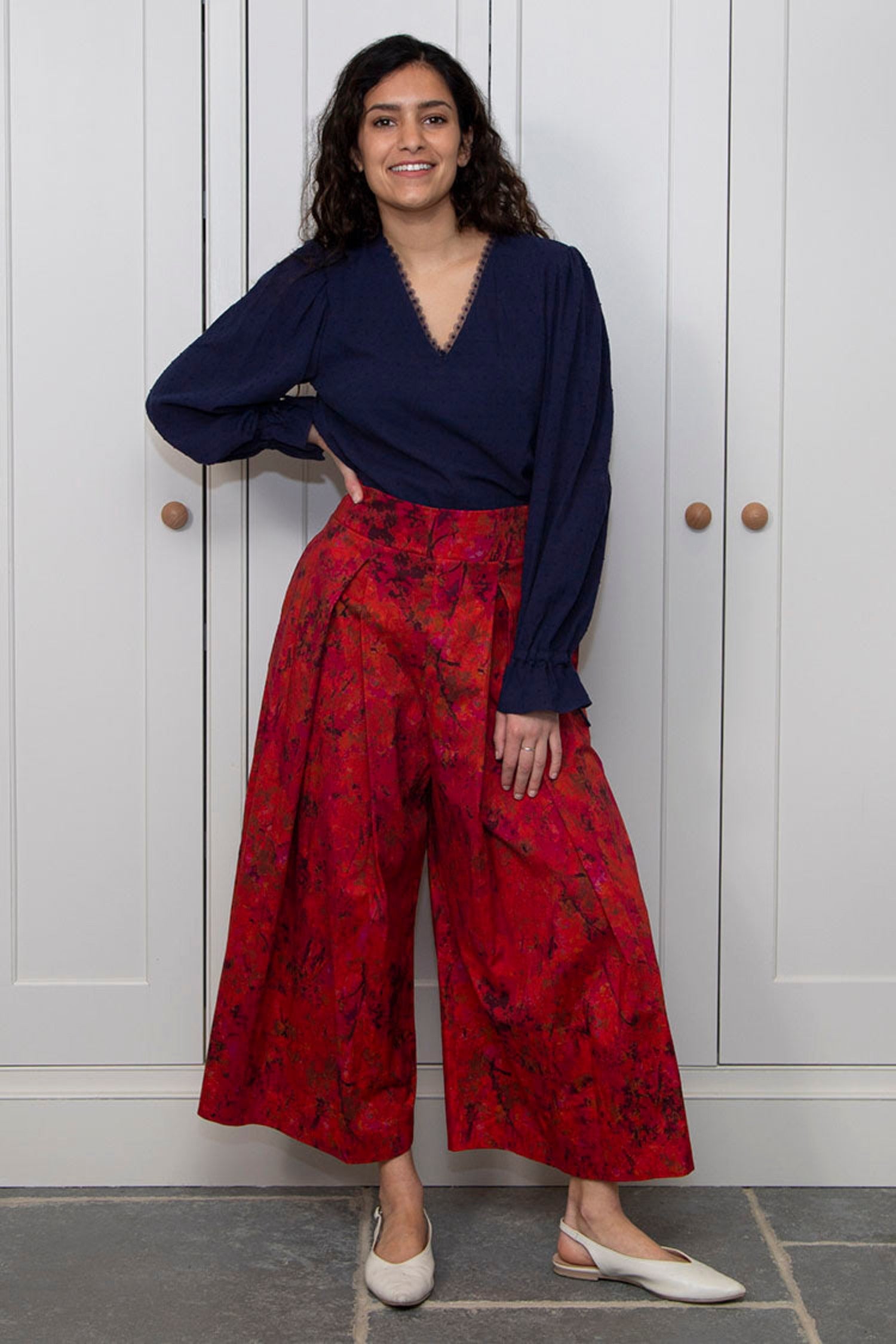 Model wearing high waisted, box pleated ¾ length silk cotton culottes in orange/red floral print, worn with navy long sleeved Maisie top.