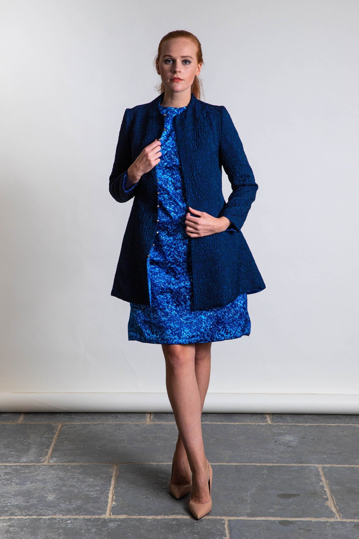 Model wearing reversible fitted A-Line navy jacquard jacket, with silver bell fastening, worn with mini A-Line dress in blue sea silk print.