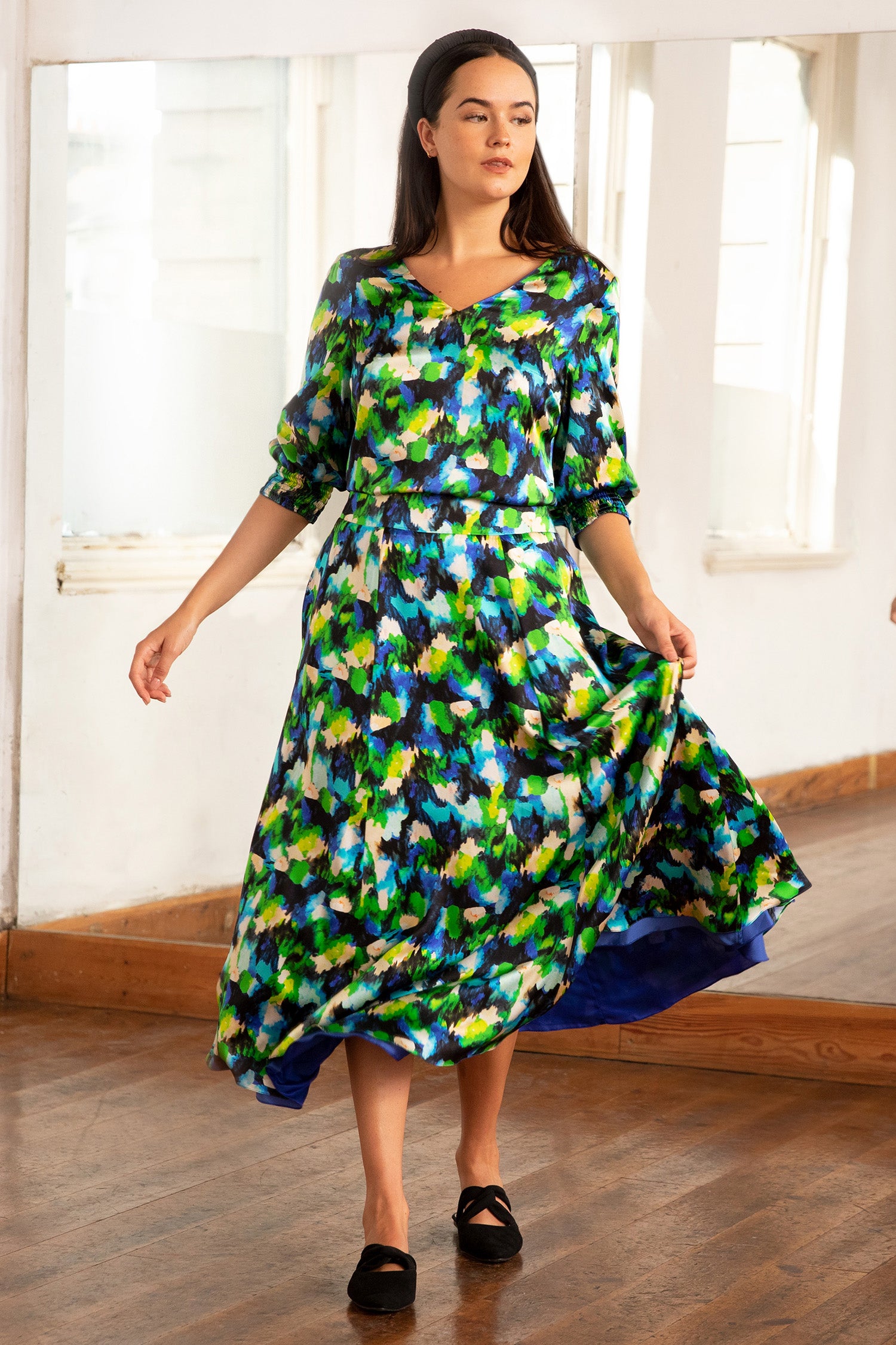 Model wearing reversible voluminous a-line midi silk satin colourful vibrant print skirt, worn with matching elbow length v-neck long sleeve top and black padded headband.