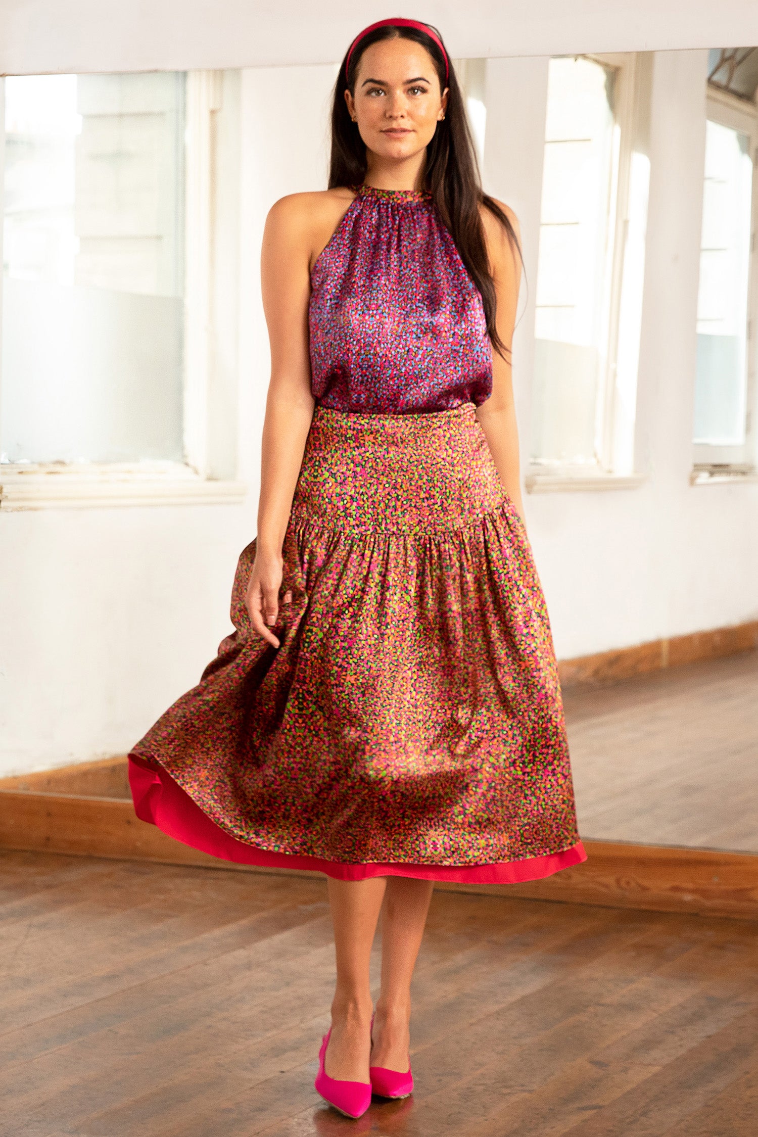 Model wearing reversible a-line midi silk satin skirt with an extra wide waistband and gathered detail from hips down in dotted orange/pink print, worn with halter neck Annie Top in Violet Dream and Raspberry Pink headband.