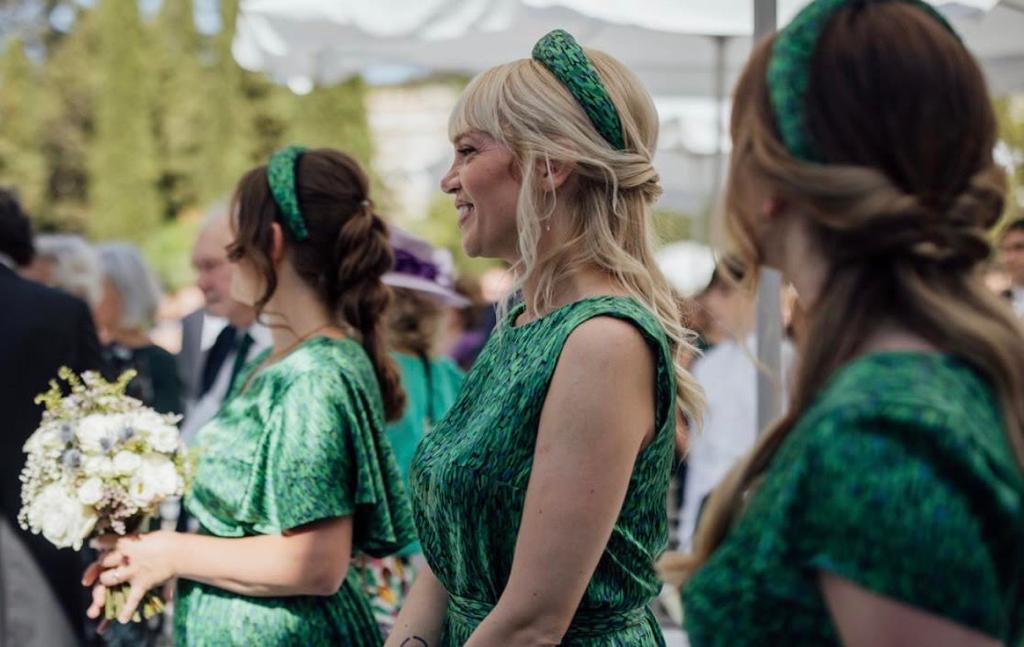 A beautiful image of three bridesmaids wearing Isabel Manns customised Flecked Emerald green silk satin dresses with matching padded headbands holding flowers at a wedding