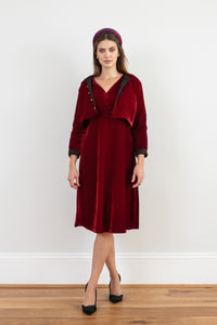 Model wearing reversible box shaped cropped burgundy velvet jacket, with gold bell fastening, worn with matching empire line Amelia dress and Fire Ocean padded headband.