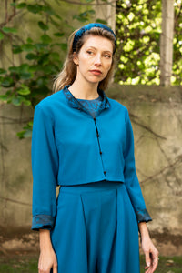 Model wearing reversible box shaped cropped teal wool crepe jacket, with mandarin collar showing contrasting silk satin reverse side and black buttons, worn with matching Penelope Trousers and Emily Top.