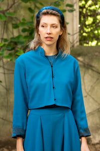 Model wearing reversible box shaped cropped teal wool crepe jacket, with mandarin collar and black buttons, worn with matching Penelope Trousers and Emily Top.