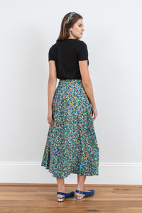 Back view of model wearing a-line midi silk bamboo green multicoloured printed skirt, worn with black v-neck t-shirt.