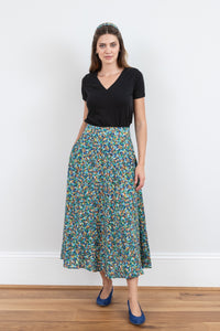 Model wearing a-line midi silk bamboo green multicoloured printed skirt, worn with black v-neck t-shirt.