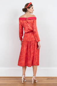 Back view of model wearing a-line midi silk bamboo skirt with an extra wide waistband and gathered detail from hips down in vibrant red swirl print, worn with matching boat neck Hayley Top and padded headband.