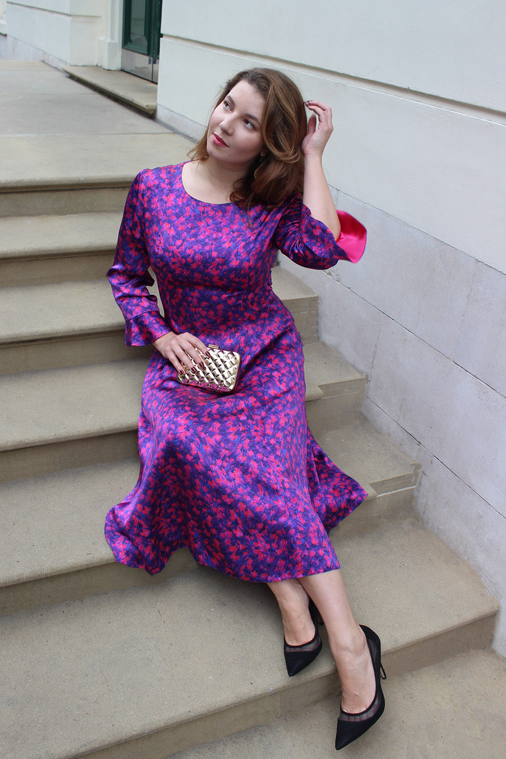 A model wearing the Ophilia silk satin dress in regal affection print and showcasing the contrast pink lining in the peplum sleeve.