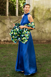 a cobalt silk satin long halter neck style dress worn by a model and waist cinched in with a tie belt, worn with a colourful vibrant printed silk satin scarf