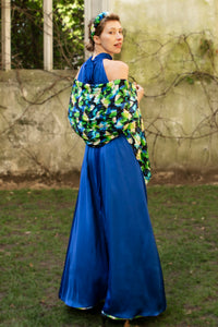 back view of a cobalt silk satin long halter neck style dress worn by a model and waist cinched in with a tie belt, worn with a colourful vibrant printed silk satin scarf