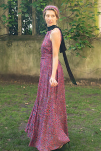 Side view of a purple dotted printed silk satin long halter neck style dress with a black collar worn by a model and waist cinched in with a tie belt