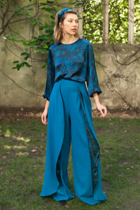 Model wearing an Isabel Manns wide leg wrap around style silk viscose trousers in teal wool crepe and contrasting teal printed silk satin lining, worn with matching silk satin long sleeve top.