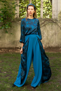 Model wearing an Isabel Manns wide leg wrap around style silk viscose trousers in teal wool crepe and contrasting teal printed silk satin lining, worn with matching silk satin long sleeve top.