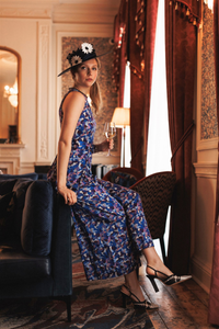 A side view of a model wearing sleeveless wide leg silk bamboo jumpsuit and matching belt that comes in a vibrant purple print with a wide brim hat.