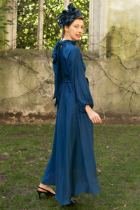 Side view of navy textured silk halter neck dress with keyhole neckline, long elasticated sleeves and a tie belt worn with a fascinator by a model