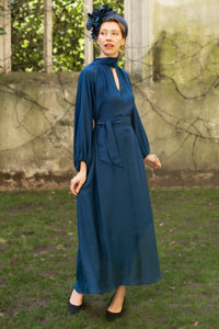 Navy textured silk halter neck dress with keyhole neckline, long elasticated sleeves and a tie belt worn with a fascinator by a model