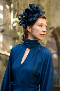 Detail shot of keyhole neckline and tie belt on navy textured silk halter neck dress, worn with a fascinator by a model