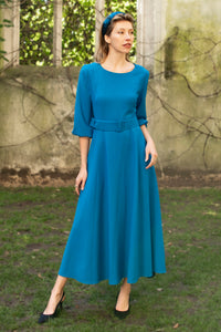 An Isabel Manns princess seam wool crepe dress in teal. Features 3/4 length elasticated sleeves, a rounded elegant neckline, and belt with buckle.