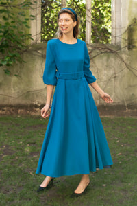 An Isabel Manns princess seam wool crepe dress in teal. Features 3/4 length elasticated sleeves, a rounded elegant neckline, and belt with buckle.