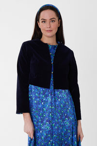 Model wearing reversible box shaped cropped navy velvet jacket, with silver bell fastening, worn with blue floral A-line Nancy Dress.