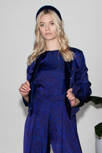 Model wearing reversible box shaped cropped dark blue silk satin/navy velvet jacket, with silver bell fastening, worn with matching Penny Jumpsuit and navy velvet padded headband.